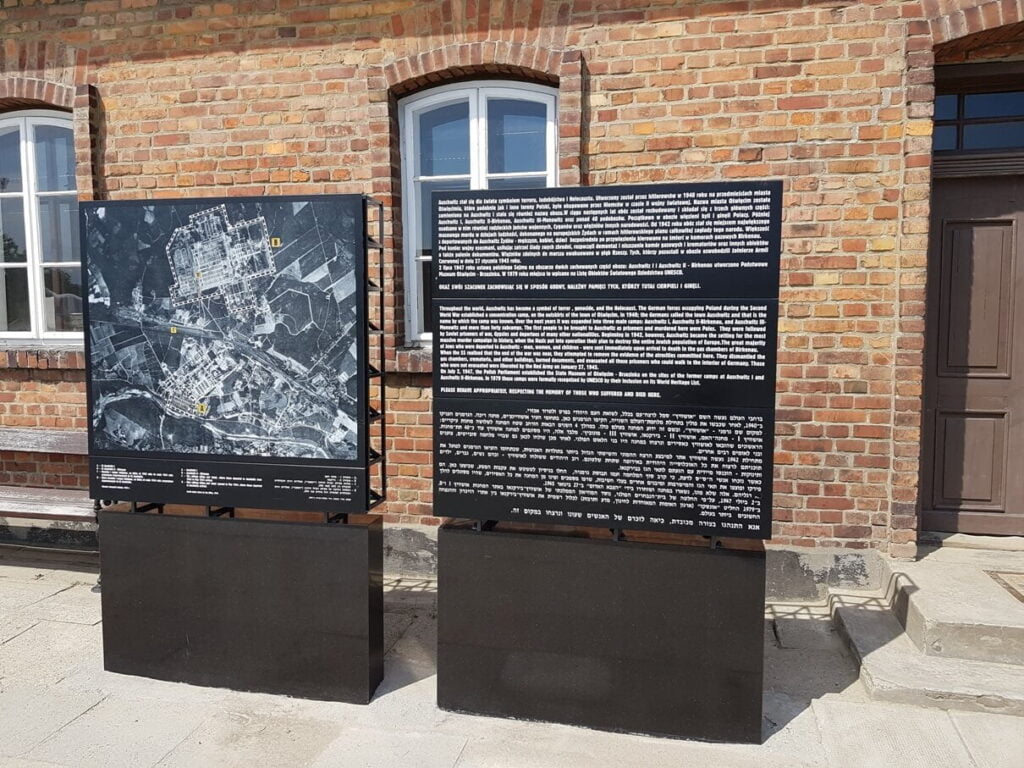 Auschwitz-Birkenau - tablica upamiętniająca i mapa obozu na tle bramy głównej do obozu